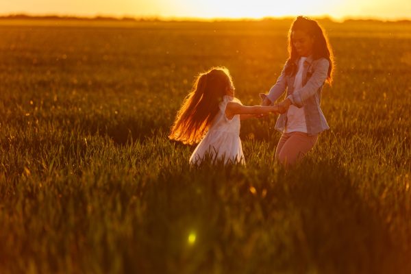 Lovely young girl playing with her mother in the fields at sunset